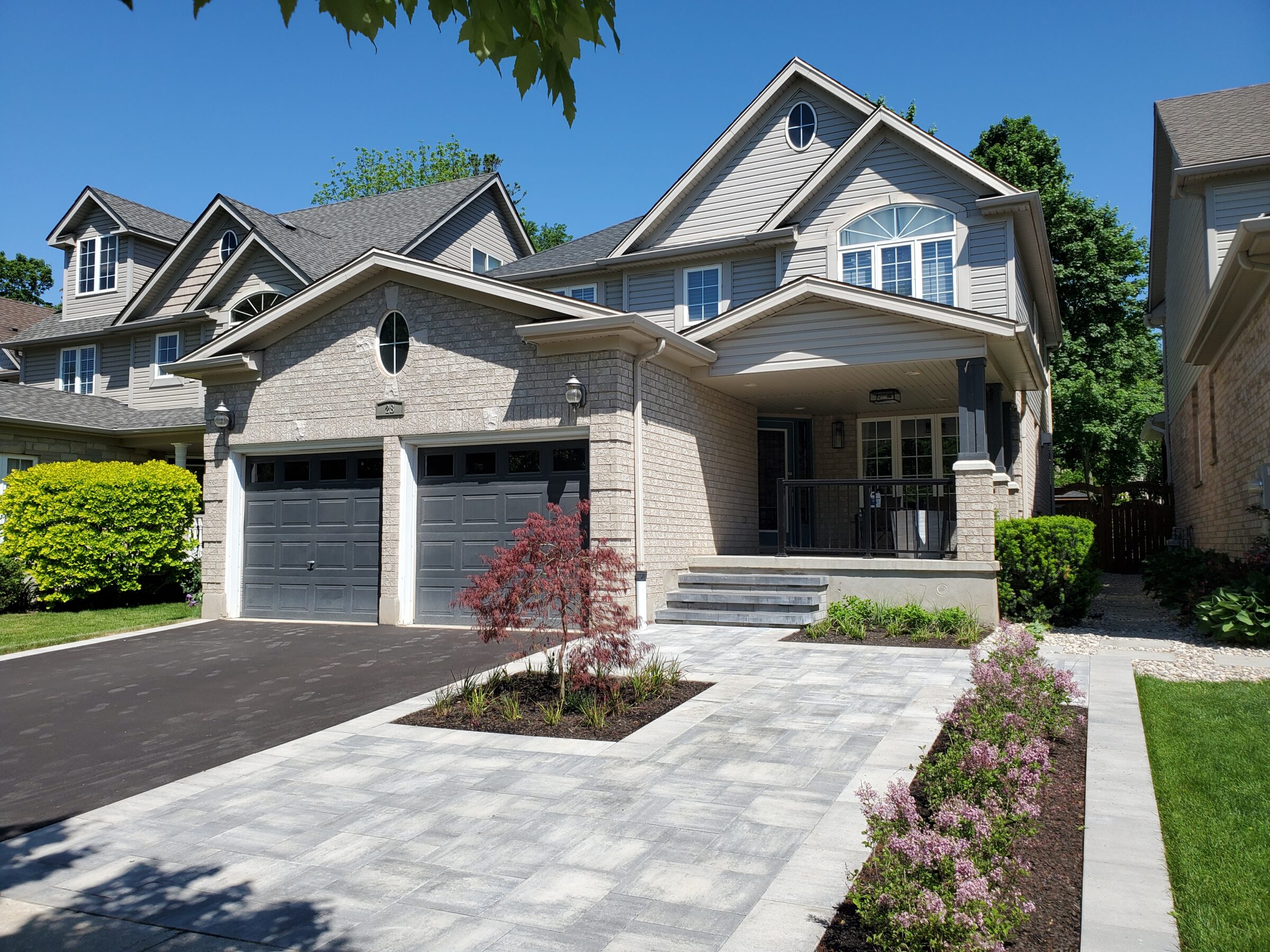 A modern suburban house with a double garage, landscaped front yard, and a stone pathway under a clear blue sky.
