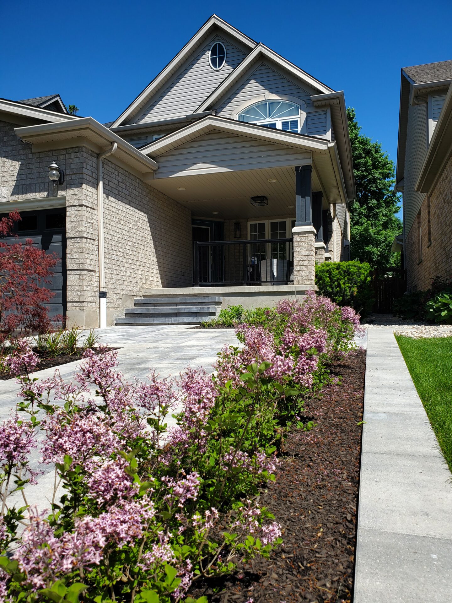 A modern house with a gabled roof, flower-lined path, and manicured lawn under a clear blue sky. No people or landmarks visible.