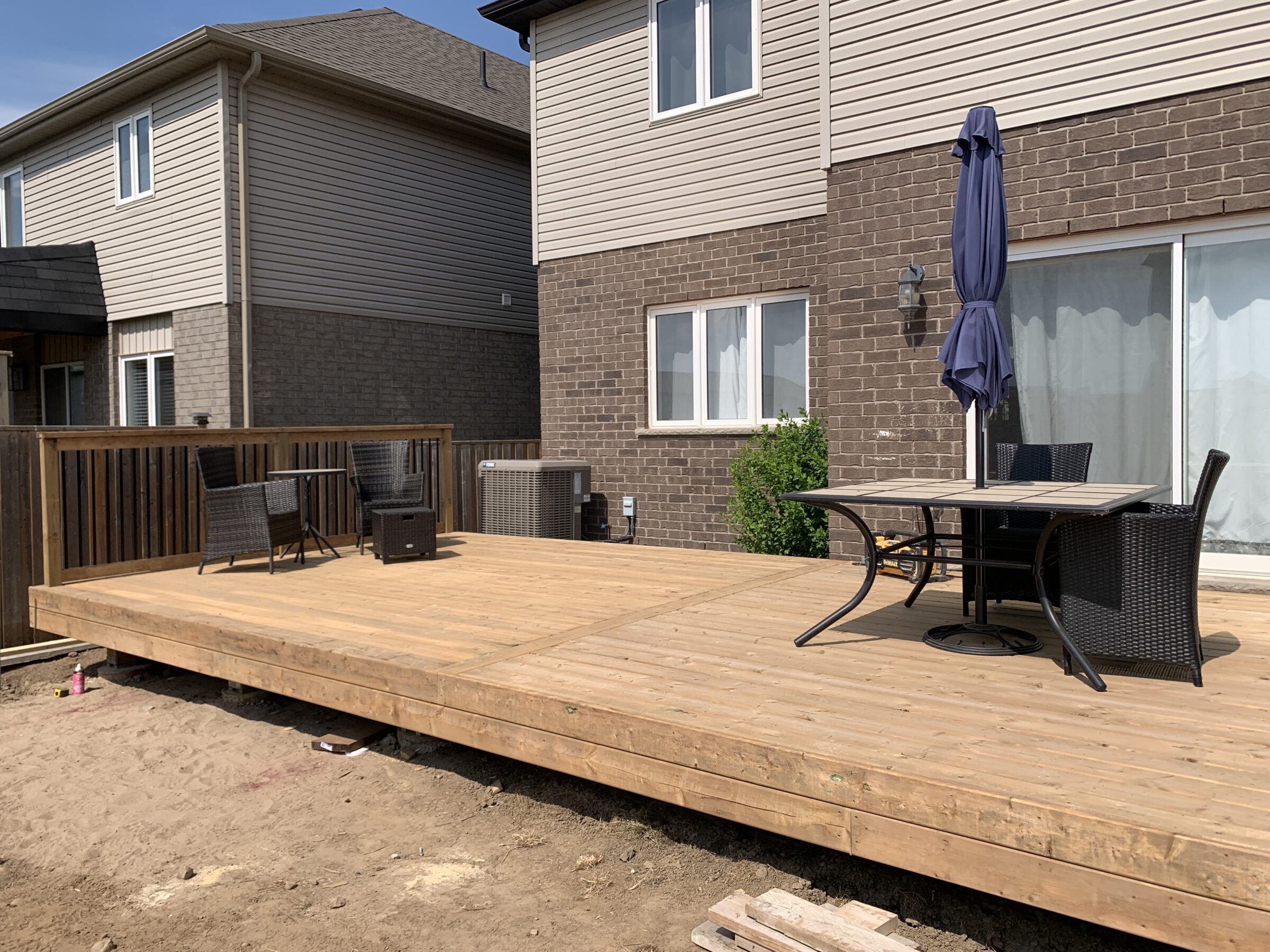 A wooden deck with wicker chairs and a table, adjacent to a brick house. No people or notable landmarks are visible.